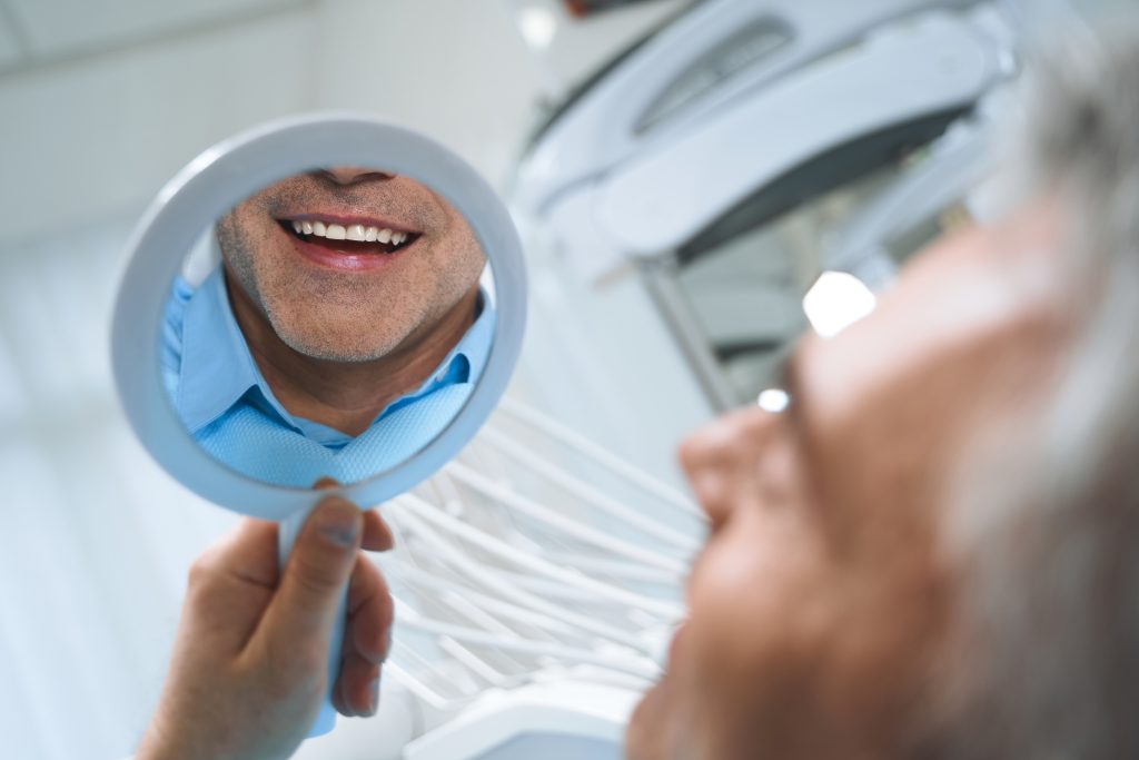 Hombre en consulta dental mirándose en el espejo para ver el resultado de su implante dental