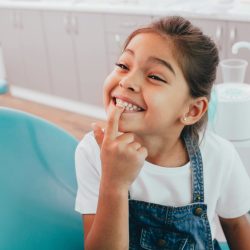 Mixed race little patient showing her perfect toothy smile while sitting dentists chair